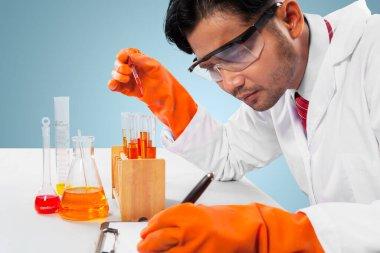 Erkek bilim adamı test tüpü tutarken ve panoya yazı yazarken bir deney yapıyor. Stüdyoda çekilmiş.