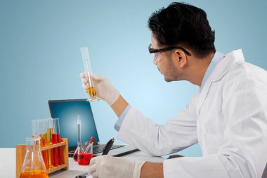 Erkek bilim adamı test tüpü tutarken ve panoya yazı yazarken tıbbi araştırma yapıyor. Stüdyoda çekilmiş.