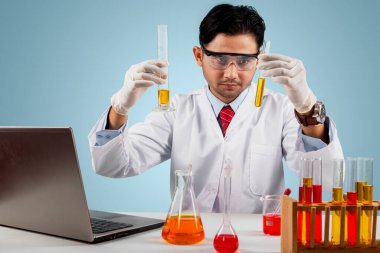 Erkek doktor, laboratuarda koronavirüs aşısı yaparken iki test tüpünü kontrol ediyor.