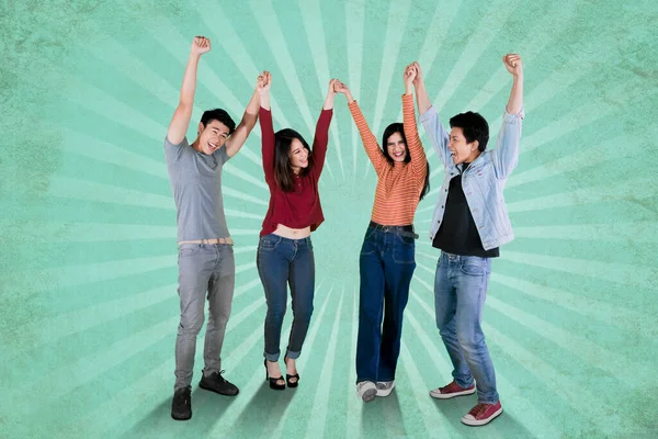緑のライトの背景で彼らの成功を祝うために一緒に手を持ち上げる幸せな人々のグループ — ストック写真