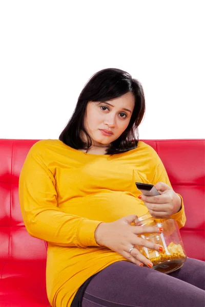 在演播室里看电视和吃薯片时 怀孕的女人看起来很无聊 — 图库照片
