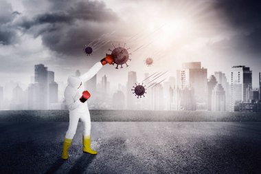 Koruyucu giysili doktor, kovid 19 veya koronavirüsü yumruklamak için boks eldiveni kullanıyor. Şehir planıyla açık havada çekilmiş.