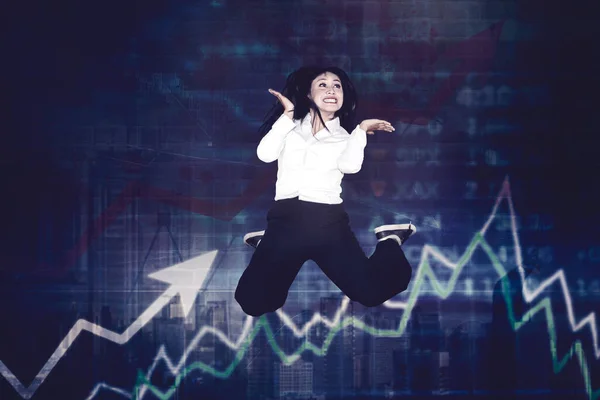 金融グラフの背景に成長してジャンプする陽気な若いビジネスマンの女性 — ストック写真
