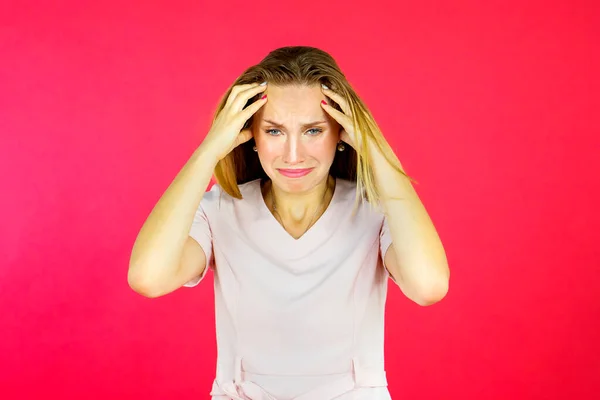 Portrait of beautiful frustrated woman standing in the studio and looks sad over red background