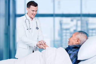 Kafkasyalı erkek doktor hastanede danışmanlık yaparken yaşlı hastasını teselli ediyor.