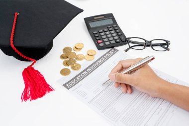 Eğitim sigortasını madeni paralarla, mezuniyet şapkasıyla ve hesap makinesiyle dolduran erkek öğrenci ellerini kapatın.