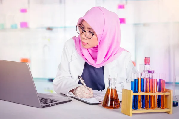 Μουσουλμάνα Γυναίκα Επιστήμονας Γράφει Ένα Πρόχειρο Κοιτάζοντας Ένα Φορητό Υπολογιστή — Φωτογραφία Αρχείου