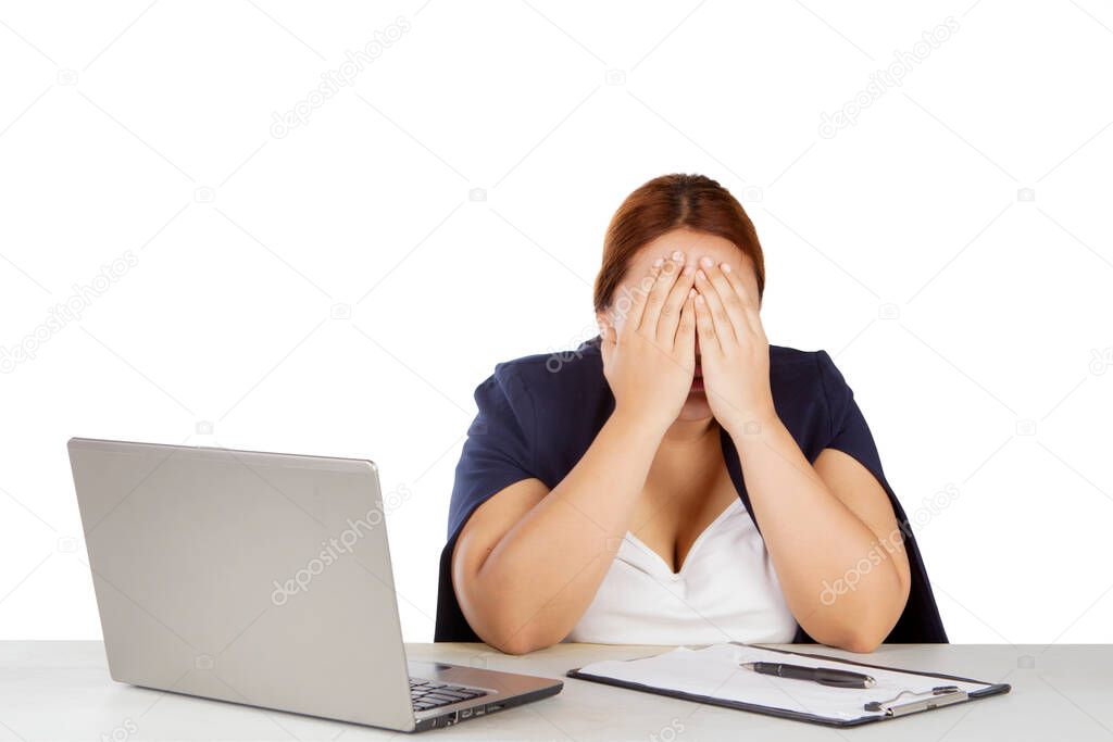 Blonde businesswoman looks sad while covering her face with hands and sitting with laptop and clipboard in the studio. Isolated on white background