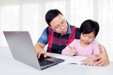 Genç baba, oturma odasında yazmayı öğrenirken kızına dizüstü bilgisayar kullanmasında yardım ediyor. Evde vuruldu.