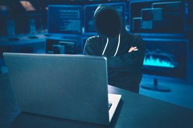 Tanımlanamayan hacker masadaki dizüstü bilgisayarla ve kodlama geçmişiyle düşünüyor.