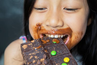 Küçük kız, ağzıyla çikolata yerken ve ısırırken mutlu görünüyor.