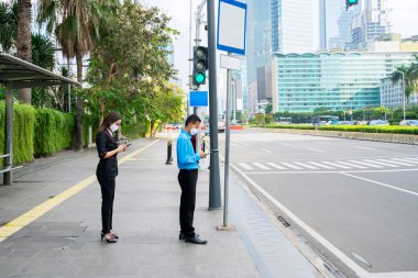 İki iş adamı yeni normal yaşam tarzında kaldırımda toplu taşıma beklerken cep telefonu kullanıyor.