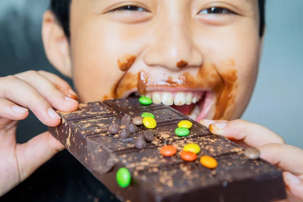 快乐的小男孩一边咬一边吃着一块巧克力 一边用凌乱的嘴看着摄像机 — 图库照片