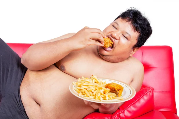 一个肥胖男人躺在沙发上吃垃圾食品时的特写镜头 在有白色背景的独立演播室里被枪杀 — 图库照片