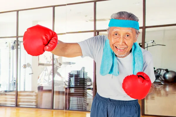 フィットネスセンターでパンチと運動を見せながらボクシンググローブを身に着けている老人 — ストック写真