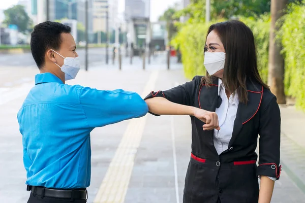 Two business people meeting and greeting with their elbow while standing on the sidewalk