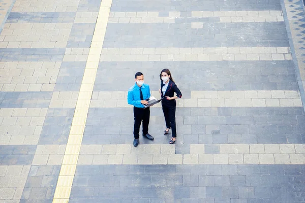 Aerial view of two business people wearing mask while looking at the camera while standing on the sidewalk