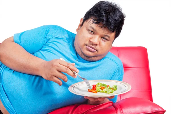 ソファに横になっている間 不幸な脂肪の男の健康的な食べ物のプレートを食べて閉じます 白い背景で隔離されたスタジオで撮影 — ストック写真