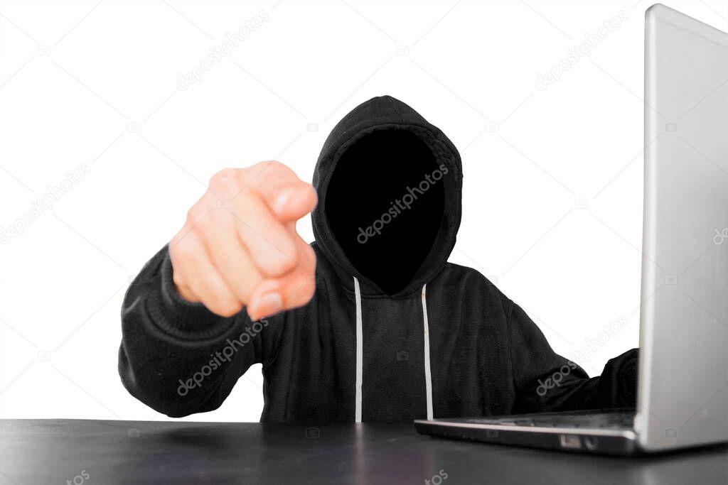 Unknown hacker pointing at the camera with laptop on desk, isolated on white background