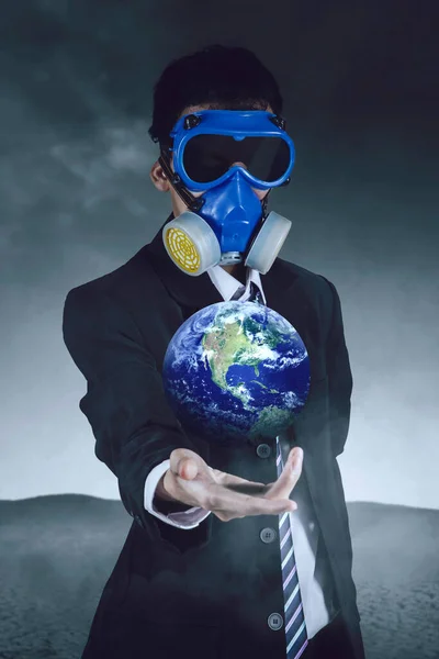 Young businessman wearing gas mask while holding a globe and standing on the desert