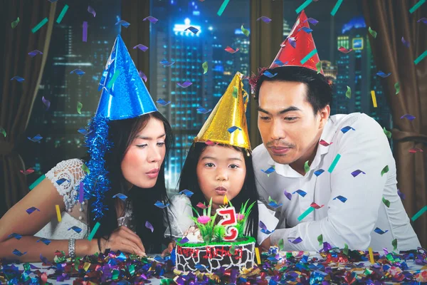 ケーキの上でろうそくを吹きながら 娘のための誕生日パーティーを祝う若い両親のイメージ — ストック写真