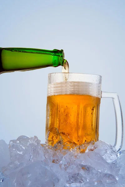 将冰镇啤酒倒入装有白色背景的冰块的杯子中 — 图库照片