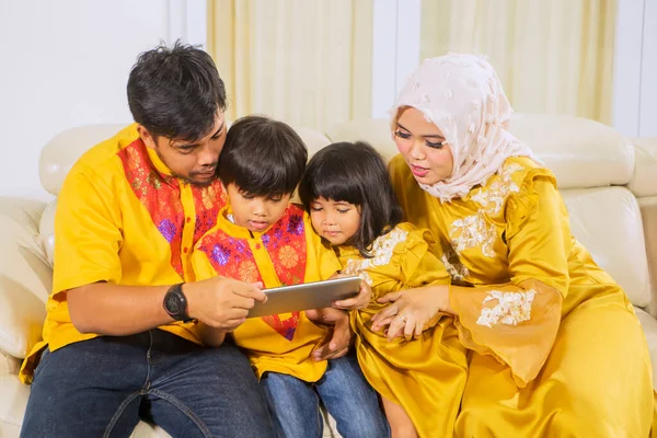 Happy muslim family playing games on a mobile phone together while sitting on the sofa in the living room at home