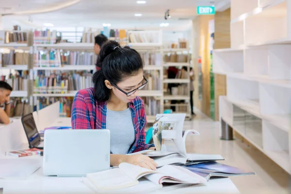 女大学生在图书馆看书的时候 用笔记本电脑学习 — 图库照片