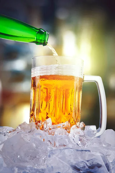 绿色瓶子将新鲜啤酒倒入装有模糊灯光背景的冰块杯中 — 图库照片