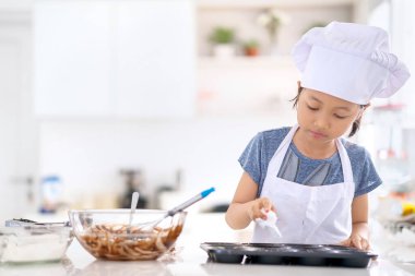 Küçük kız mutfakta dururken kurabiye hamuruna krema eklemek için pasta poşeti kullanıyor. Evde vuruldu.