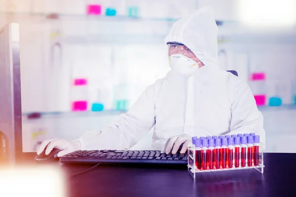 在实验室与计算机和试管一起工作时 男性科学家穿着危险垫套装 — 图库照片