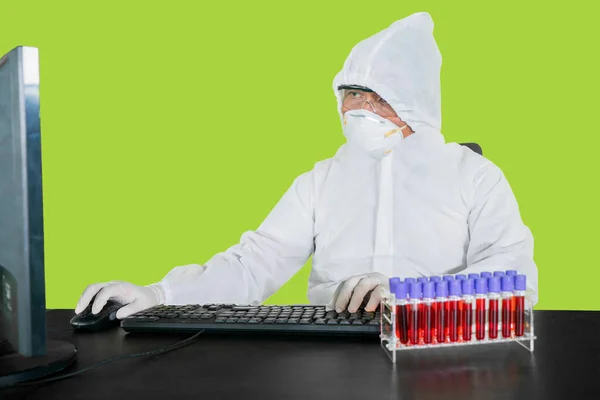 Medical worker in protective suit while using a computer and sitting with green screen background