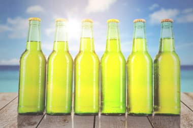 Sıranın başında açılmamış taze bira şişeleri ve kumsaldaki mavi gökyüzünün altında damlalar var.
