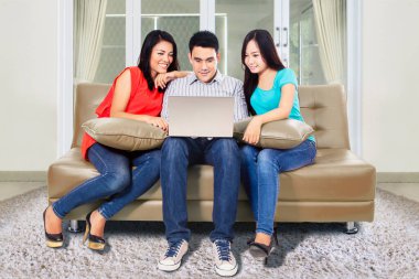 Oturma odasında kanepede yan yana otururken dizüstü bilgisayar kullanan bir grup neşeli genç. Evde vuruldu.