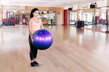 Spor kıyafetleri giyen Hintli bir kadın yoga topu tutuyor ve spor salonunda egzersiz yapıyor.