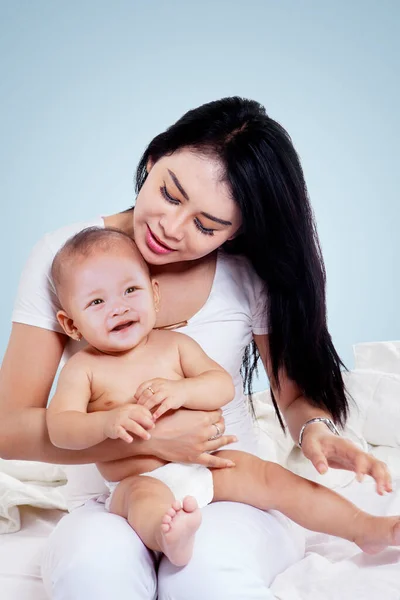 幸せな若いですお母さん抱擁彼女の赤ん坊ながら一緒にプレイでザ スタジオでグレー色の背景 — ストック写真