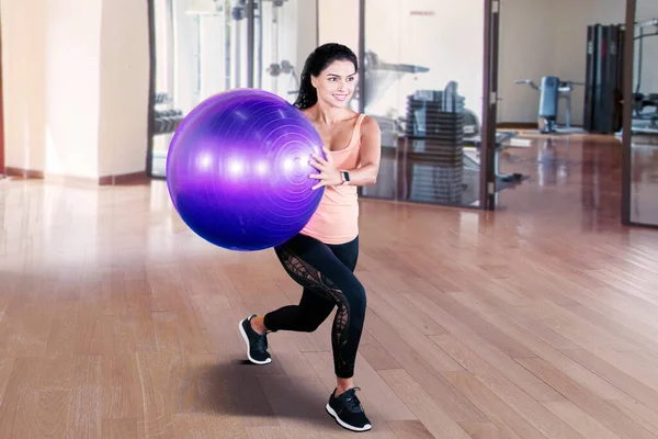 Genç Hintli kadın spor kıyafetlerini spor salonunda yoga topuyla egzersiz yaparken giyer.