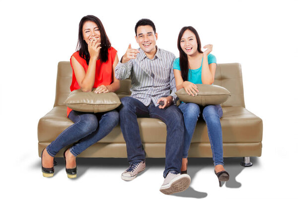 Three happy young people watching comedy movie on the TV while sitting together on the couch. Isolated on white background