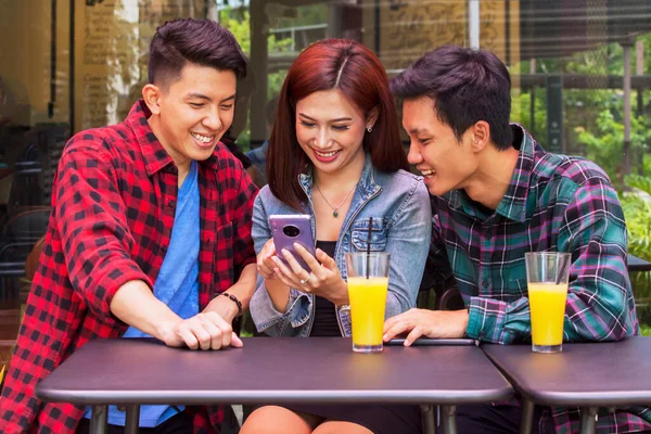 Group of young people sitting in cafe while talking and using a mobile phone together