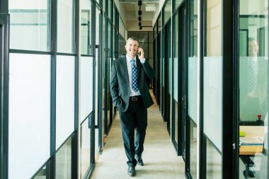 Erkek yönetici kameraya gülümserken bir telefon eder ve ofis koridorunda durur.