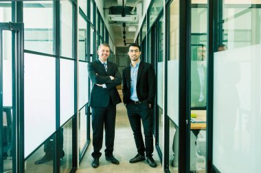 Ofis koridorunda kameraya gülümseyen iki kendine güvenen işadamı.