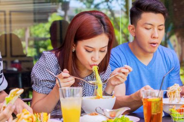 Lokantada arkadaşlarıyla yemek yerken bir kase erişte yiyen genç bir kadının yakın çekimi.