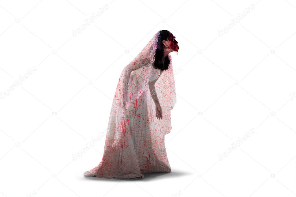 Halloween horror concept. Side view of horrible female ghost wearing bloody bride gown and walking in the studio