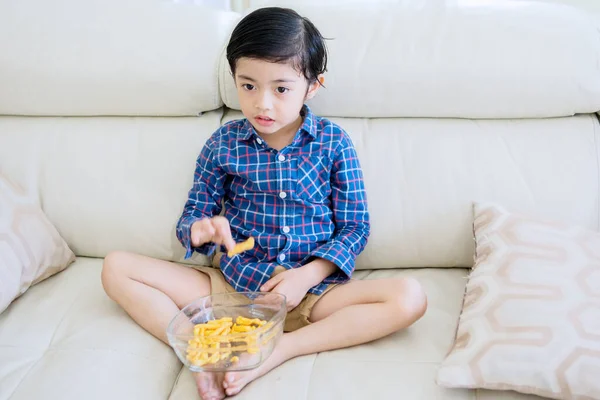 可爱的小男孩一边吃着一碗点心 一边在沙发上放松 一边换频道电视 在家里中弹 — 图库照片