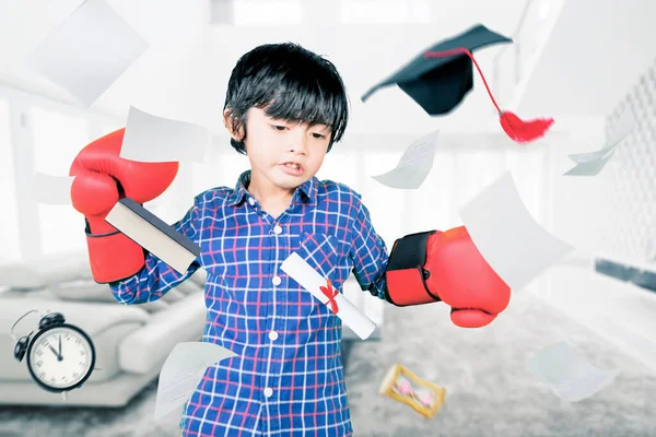 愤怒的小男孩带着拳击手套在家里的卧室里抛出了文件和毕业帽 — 图库照片