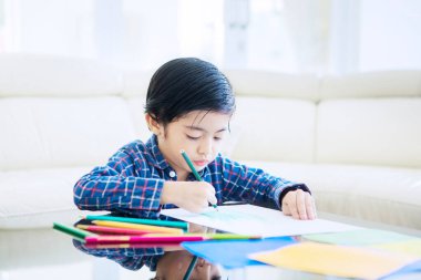 Coronavirus yüzünden evde karantina yaparken kağıda resim çizen sevimli bir çocuk. Oturma odasında vurulmuş.