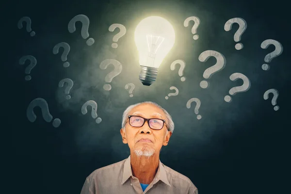 Picture of old man looking at a bright bulb while standing under question marks symbol