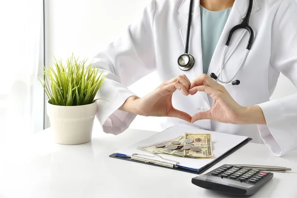 Medical and health insurance concept, Doctor doing hand heart shape gesture with money in hospital background, Money saving for medical care expenses.