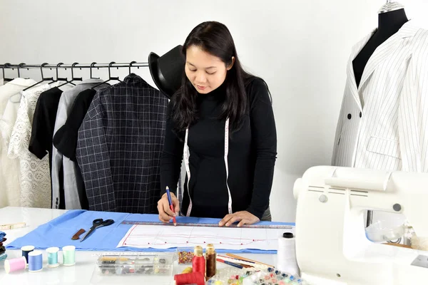 Small business owner, Dressmaker designer making pattern and measure garment, Asian fashion designer working in her showroom studio.