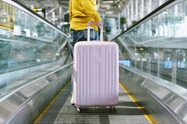 Kadın gezgin, havaalanı terminalindeki yürüyen merdivende büyük bir bavul taşıyor, yolcu, çıkış gişesine bavulla yürüyor, turist varış noktasına varıyor, seyahat konsepti....